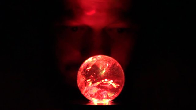 A man looks into a glowing ball of glass looking for divination of the future.