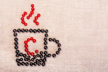 Berries of black and red currants isolated on sackcloth. Health, vitamins and diet concept. Berries placed in the form of a cup with vitamin C. Top view. Free space inscription field.