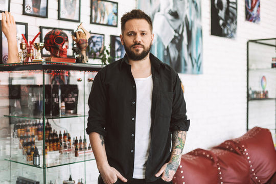 Young tattooer dreamily looking in camera spending time in tattoo studio
