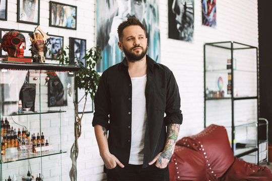 Young tattooer in black shirt thoughtfully looking aside spending time in tattoo studio