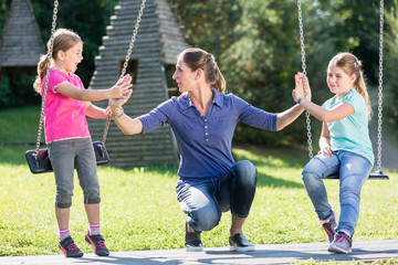 Happy family with two girls and mother on playground swing