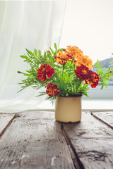 bouquet of orange flowers in an iron mug on the table near the window in a vintage style with a copy space