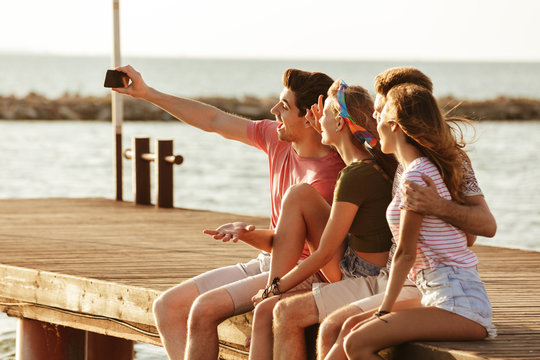 Friends sitting outdoors on the beach take a selfie.