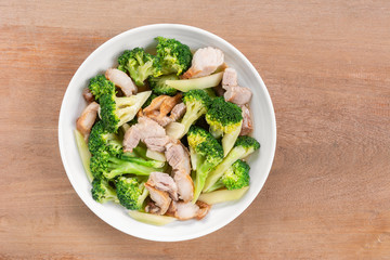 top view of stir fried pork belly and broccoli with soy sauce in a ceramic dish on wooden table. homemade style food concept.