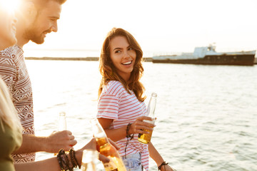 Happy young friends outdoors on the beach drinking beer.