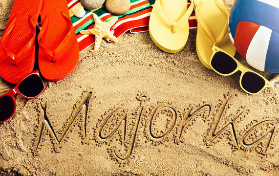 Summer concept of sandy beach, colorful thongs shoes, sunglasses, ball and inscription majorka
