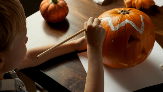 Young boy carving and painting a pumpkin for Halloween on a table