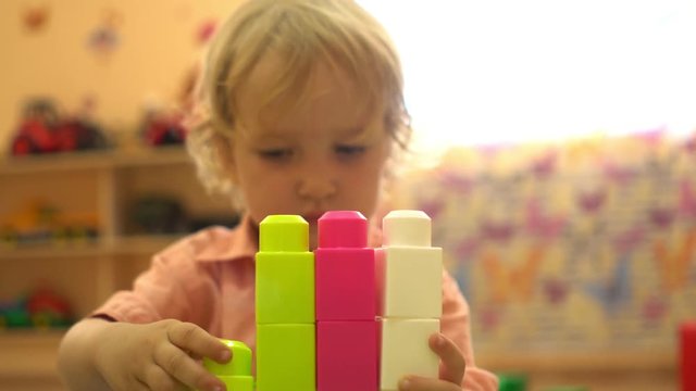 Preschool happy child playing with multi coloured building blocks in nursery school