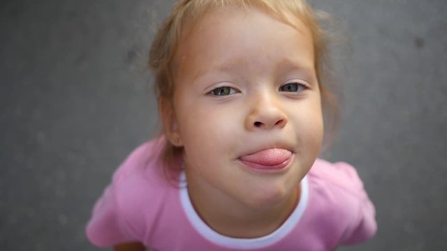 Little child girl face portrait grimace show tongue to camera slow motion