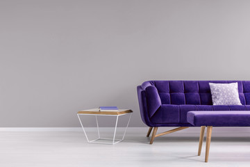 Pillow on a stylish, vibrant purple settee and a diamond shape, side table in a gray living room...