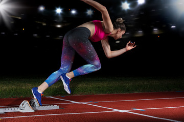 woman sprinter leaving starting blocks on the athletic track. exploding start on stadium with...
