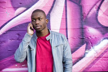 Portrait of a hot black man in front of graffiti wall, using cell phone, posing for camera