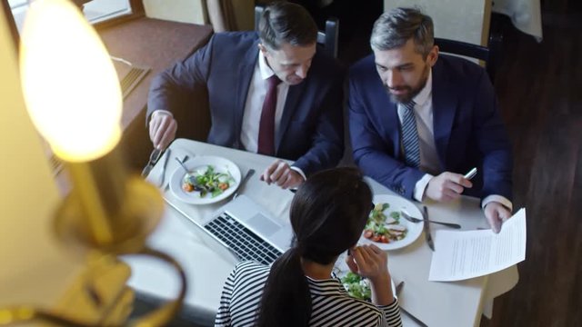 High angle view of three colleagues discussing contract when sitting at table in cafe or restaurant and having business lunch