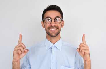 Horizontal closeup shot of happy satisfied Caucasian male points upwards with both index fingers,...