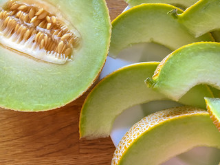 Half melon and melon slice on white plate on wooden table. closeup
