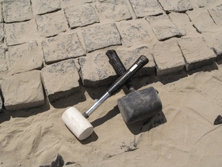 Two crossed rubber hammers lie on the unfinished laying of granite paving stones. Building...
