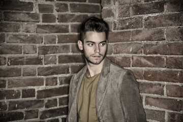 Attractive young man standing against brick wall, looking away to a side