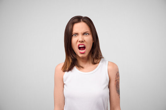 Furious angry woman screaming with rage and frustration. Negative human emotions, face expressions. Portrait of a frustrated angry woman screaming out loud out isolated on the gray background