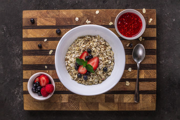 Porridge with blueberries, raspberries and strawberries, raspberry jam and mint leaves on a wooden background. Healthy eating. Breakfast