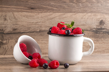Berries of juicy raspberries and blueberries in a white cup on a wooden background