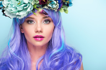 close-up portrait of beautiful young woman with curly blue hair and floral wreath isolated on blue