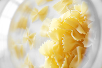 Uncooked Italian farfalle pasta, on a white background. Raw pasta is scattered around the trasparent glass. Flour products.