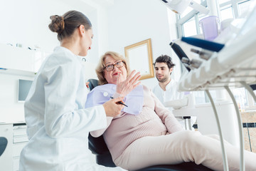 Dentist and assistant greeting senior patient in their surgery 