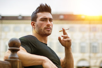 Handsome masculine adult man looking at camera while sitting and smoking. 
