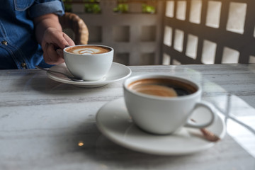 Closeup image of a hand holding a white cup of hot latte coffee on table in cafe