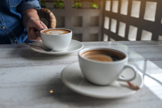 Closeup image of a hand holding a white cup of hot latte coffee on table in cafe