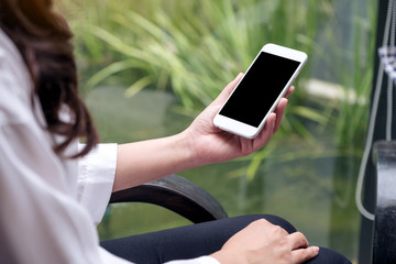 Mockup image of a woman holding white smart phone with blank black desktop screen with blur green nature background
