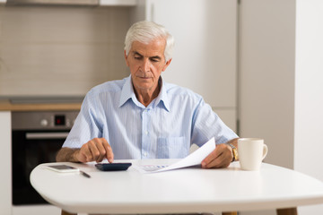Elderly man sitting at home and calculating bills and taxes.