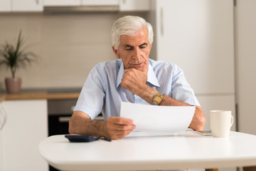 Elderly man sitting at home and calculating bills and taxes.