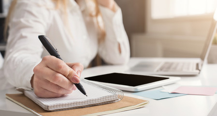 Young successful woman writing notes while sitting in office