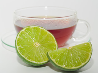 Eine Tasse Tee, davor liegen eine halbe und eine viertel Limette 