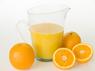 ein Glaskrug mit Orangensaft, davor liegen Orangen 