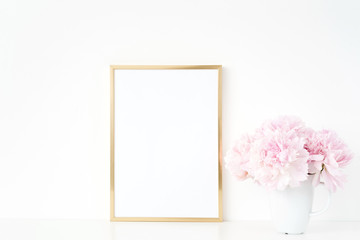 Gold portrait a4 frame mockup template with peonies in vase on white background. Empty frame mock...