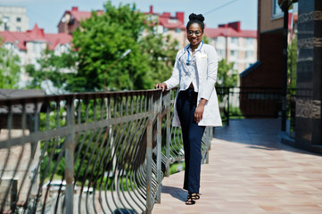 African american doctor female at lab coat with stethoscope posed outdoor against clinic.