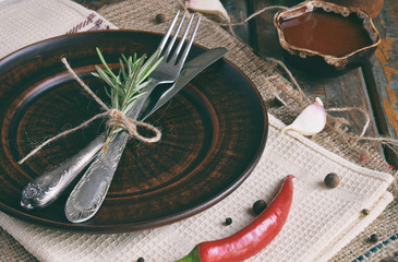 Rustic table setting with clay plate, cutlery, pepper mill, bottles of wine, greens, vegetables and...