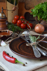 Rustic table setting with clay plate, cutlery, pepper mill, bottles of wine, greens, vegetables and spices. Country style. Copy space for text