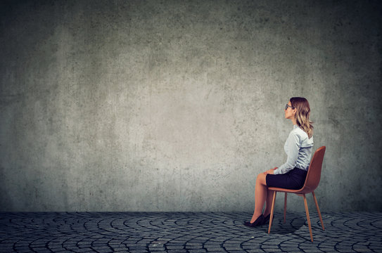 Business woman sitting on a chair in front of a wall and thinking