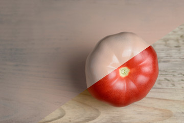 Natural red and beige or ecru half painted tomato on wooden background.