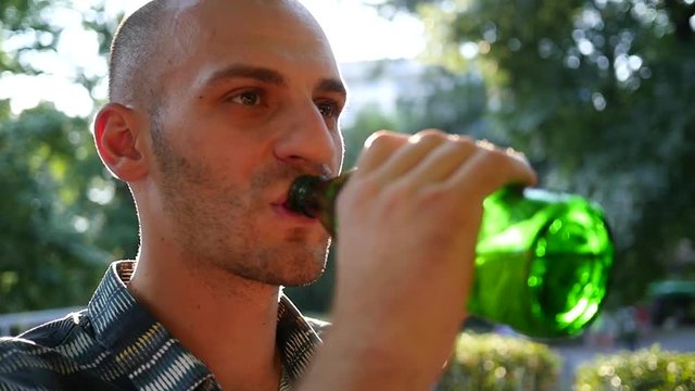 Man drinking alcohol beer from bottle outdoors in park in sun back light haze slow motion