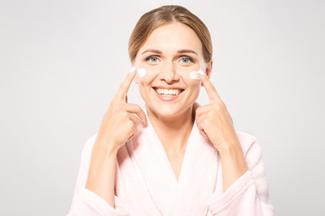 Portrait of young beautiful woman smiling while taking some facial cream isolated on white background with copy space.