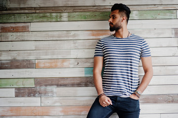 Handsome tall arabian beard man model at stripped shirt posed outdoor against wooden background....