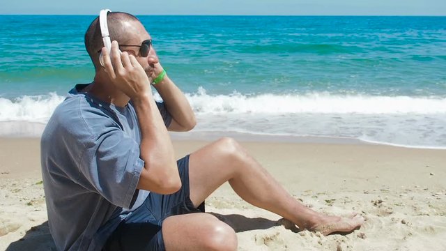 A man on the beach listening to music. A man in headphones sits on the sand by the sea.