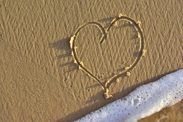 heart on a sand of beach with wave on background