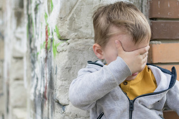 Plakat Depression in a young child. A little boy is sitting in a dilapidated old building, covering his face with his hands.