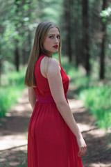 Blonde woman in red dress in forest looking over shoulder.