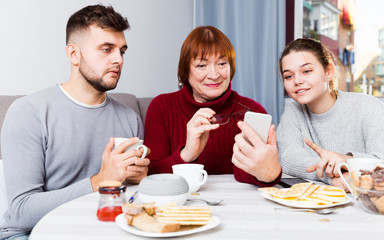 Senior woman with adult children using mobile gadget
